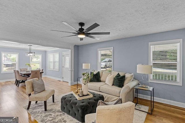 living room with baseboards, a textured ceiling, light wood-type flooring, and a healthy amount of sunlight