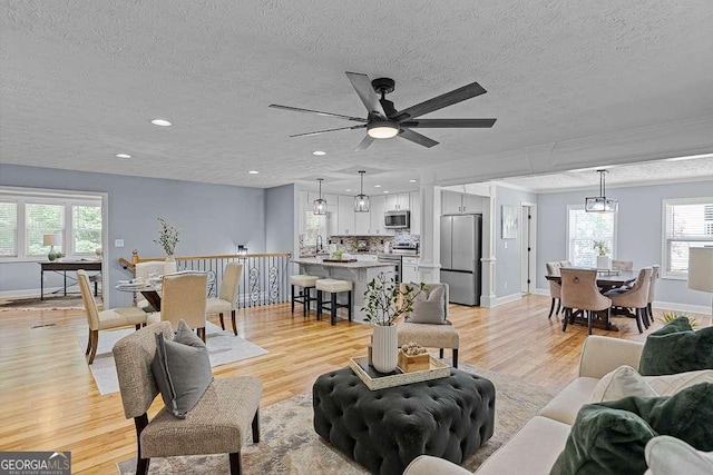 living area with light wood-style floors, baseboards, a textured ceiling, and recessed lighting