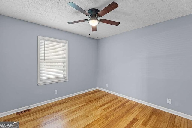 empty room with a textured ceiling, wood finished floors, and baseboards