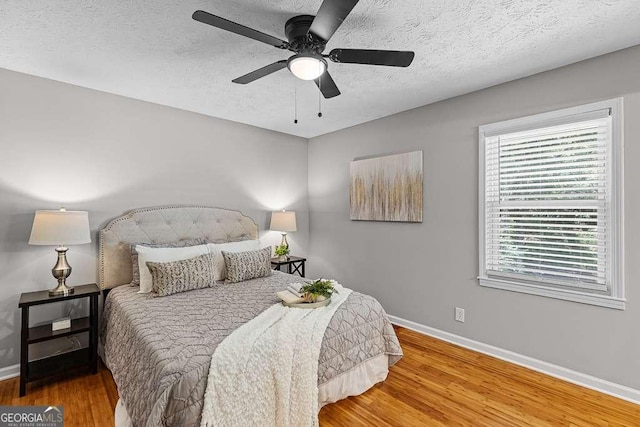 bedroom featuring a ceiling fan, a textured ceiling, baseboards, and wood finished floors