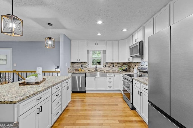 kitchen with light wood finished floors, stainless steel appliances, backsplash, white cabinetry, and a sink