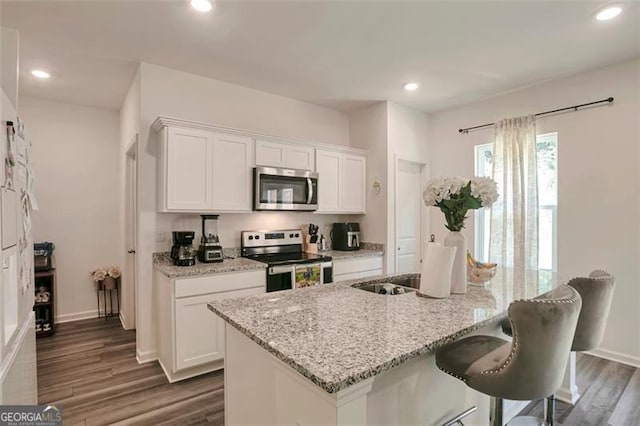 kitchen with light stone countertops, white cabinets, appliances with stainless steel finishes, dark wood-type flooring, and a kitchen island with sink