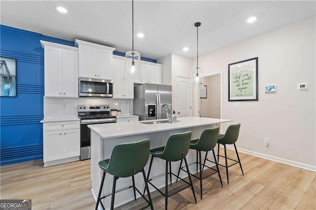 kitchen featuring stainless steel appliances, tasteful backsplash, light wood-style flooring, a kitchen island with sink, and a sink