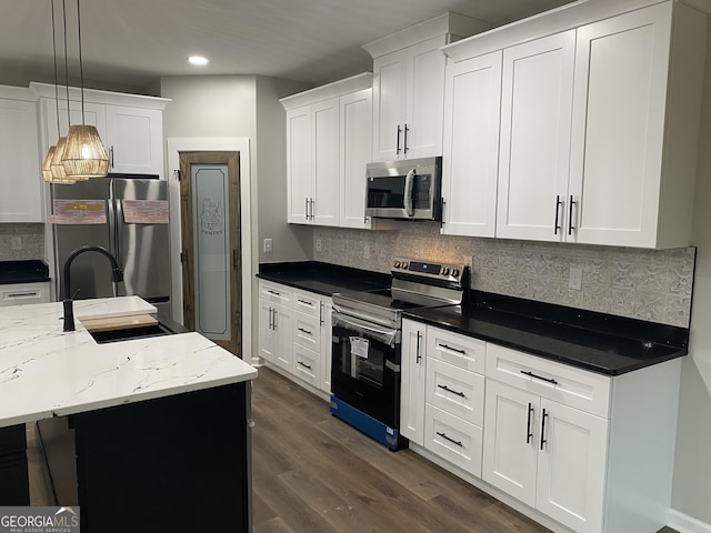 kitchen featuring decorative light fixtures, dark stone countertops, appliances with stainless steel finishes, an island with sink, and white cabinets