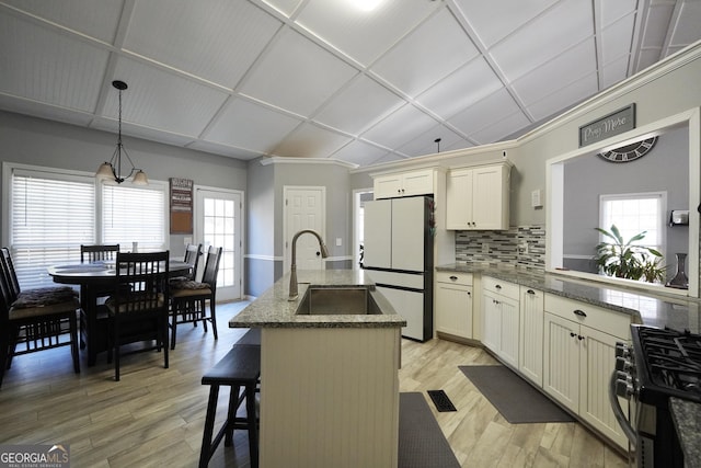 kitchen with light hardwood / wood-style flooring, range with gas stovetop, a kitchen island, decorative light fixtures, and white fridge