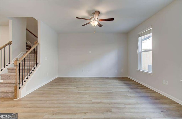 empty room with stairway, ceiling fan, light wood-style flooring, and baseboards