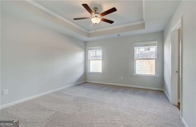 carpeted spare room featuring baseboards, visible vents, a raised ceiling, and crown molding