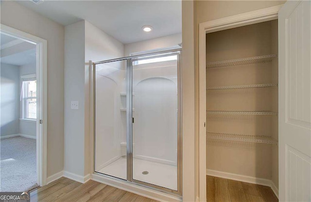 full bath featuring a shower stall, a spacious closet, baseboards, and wood finished floors