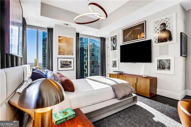 bedroom with a tray ceiling, dark hardwood / wood-style flooring, and a wall of windows