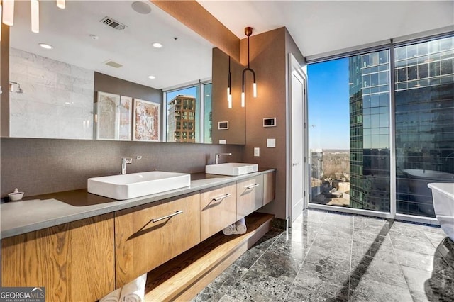 full bathroom with a freestanding bath, double vanity, visible vents, and a sink