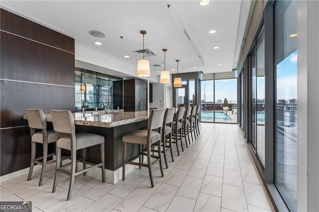 kitchen with light stone counters, decorative light fixtures, a wall of windows, and a breakfast bar