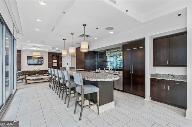 kitchen featuring light stone countertops, pendant lighting, dark brown cabinetry, a center island, and paneled built in refrigerator