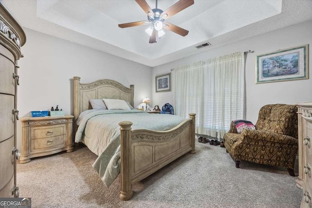 bedroom with light carpet, ceiling fan, and a raised ceiling