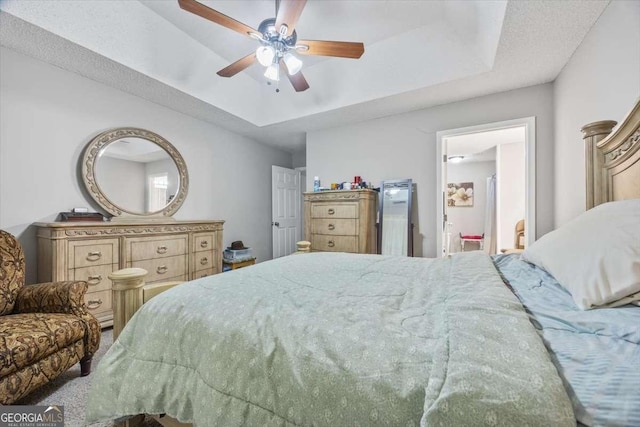 bedroom featuring ceiling fan, a tray ceiling, and ensuite bath