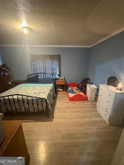 bedroom with light wood-type flooring, ornamental molding, and a textured ceiling