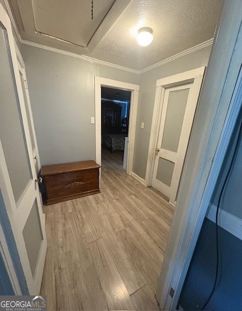 corridor with a textured ceiling, crown molding, and light wood-type flooring