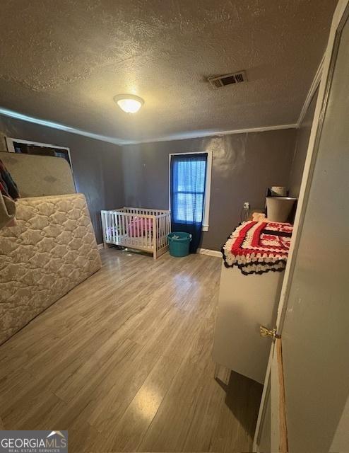 bedroom with crown molding, a textured ceiling, and wood-type flooring