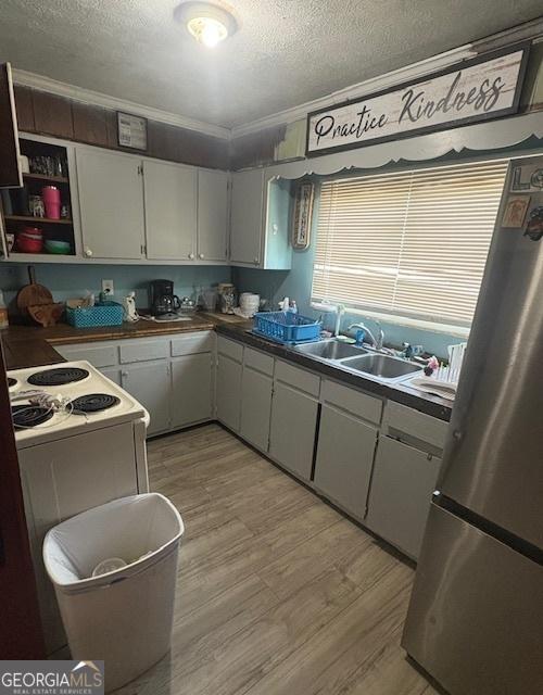 kitchen with a textured ceiling, light hardwood / wood-style floors, sink, stainless steel fridge, and ornamental molding