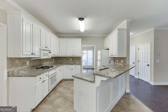 kitchen with white appliances, white cabinets, ornamental molding, kitchen peninsula, and light stone counters