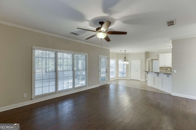 unfurnished living room featuring ceiling fan with notable chandelier, a wealth of natural light, dark hardwood / wood-style floors, and ornamental molding