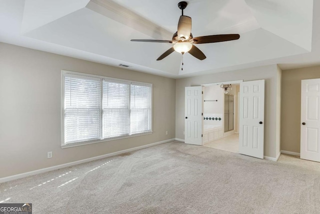 unfurnished bedroom with ceiling fan, light colored carpet, and a tray ceiling