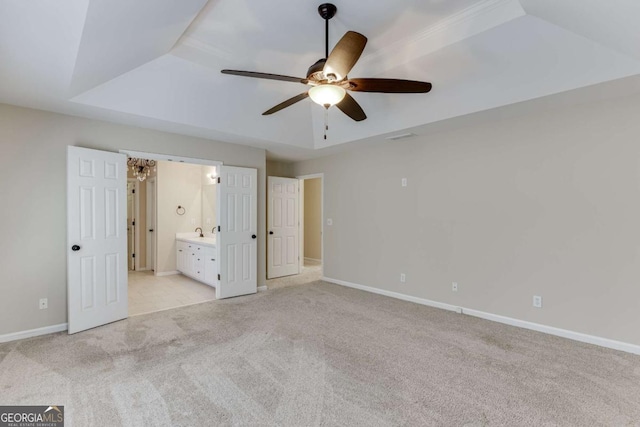 unfurnished bedroom featuring ceiling fan, ensuite bathroom, a raised ceiling, and light carpet