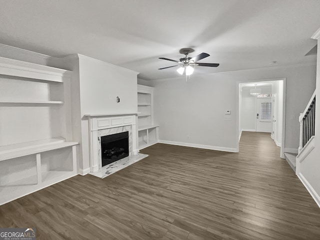 unfurnished living room with a premium fireplace, ceiling fan, crown molding, and dark wood-type flooring