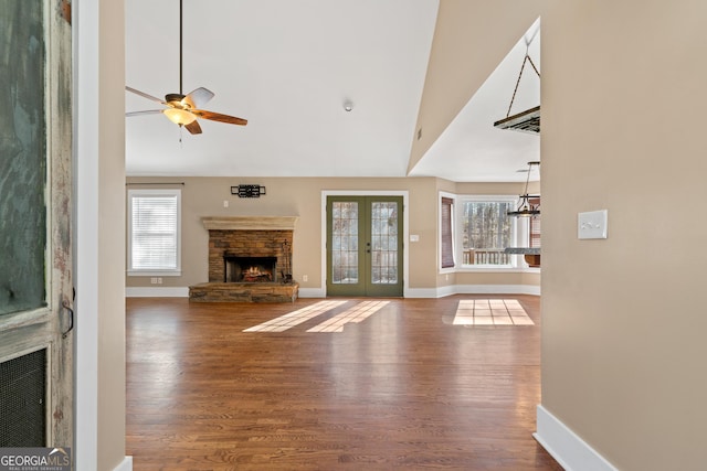 unfurnished living room with vaulted ceiling, wood-type flooring, a stone fireplace, and french doors