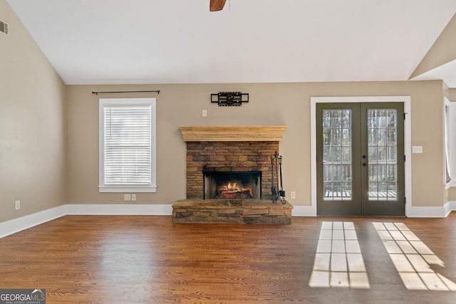 unfurnished living room with french doors, wood-type flooring, a stone fireplace, and vaulted ceiling