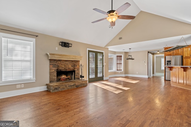 unfurnished living room featuring high vaulted ceiling, a fireplace, hardwood / wood-style flooring, ceiling fan, and french doors