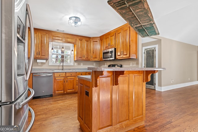 kitchen with stainless steel appliances, hardwood / wood-style flooring, a kitchen bar, and kitchen peninsula