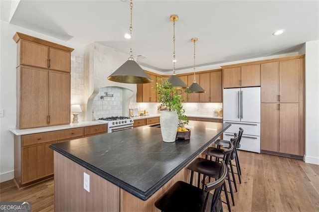 kitchen with light hardwood / wood-style flooring, hanging light fixtures, stainless steel stove, a center island, and white fridge