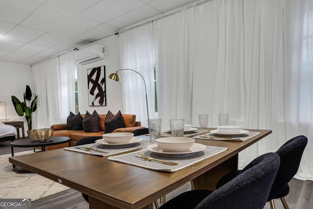 dining area with an AC wall unit, a paneled ceiling, and wood-type flooring