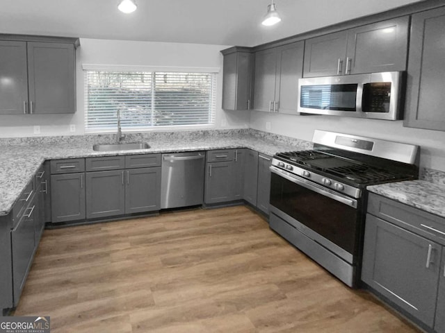 kitchen with wood-type flooring, gray cabinetry, sink, stainless steel appliances, and light stone counters