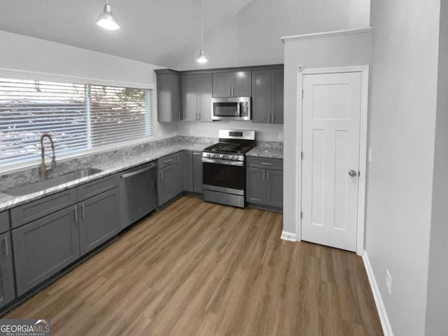 kitchen featuring pendant lighting, stainless steel appliances, sink, gray cabinets, and vaulted ceiling