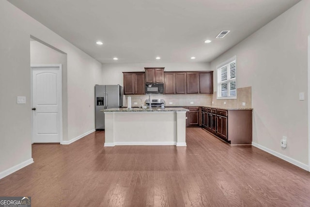 kitchen featuring hardwood / wood-style flooring, decorative backsplash, stainless steel fridge with ice dispenser, and an island with sink