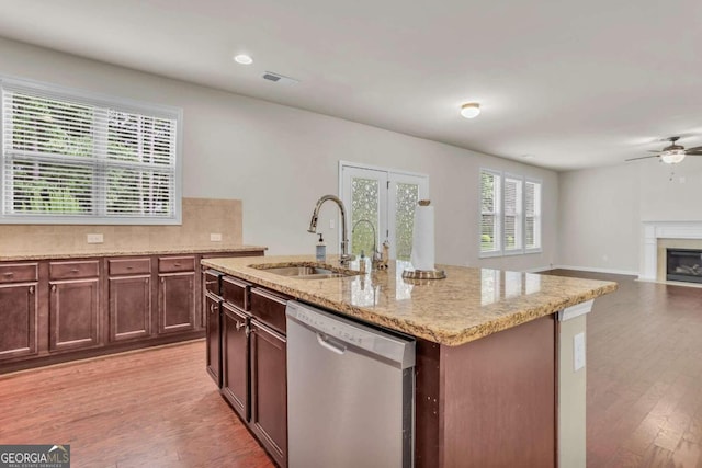kitchen with dishwasher, decorative backsplash, sink, light wood-type flooring, and a center island with sink
