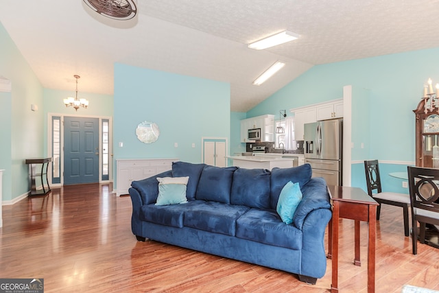 living room with vaulted ceiling, sink, a chandelier, light hardwood / wood-style floors, and a textured ceiling