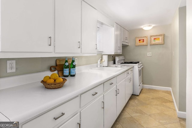 kitchen featuring white gas range, white cabinets, and sink