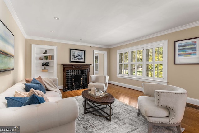 living room with wood-type flooring, built in features, a tiled fireplace, and ornamental molding