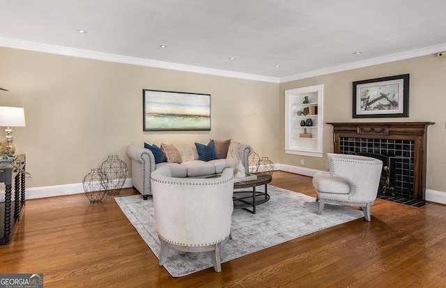 living room featuring built in shelves, crown molding, hardwood / wood-style floors, and a tiled fireplace