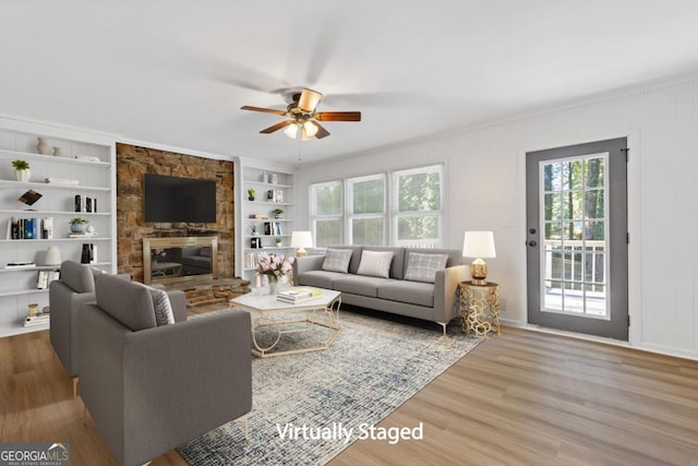 living room with built in shelves, a wealth of natural light, a fireplace, and wood-type flooring