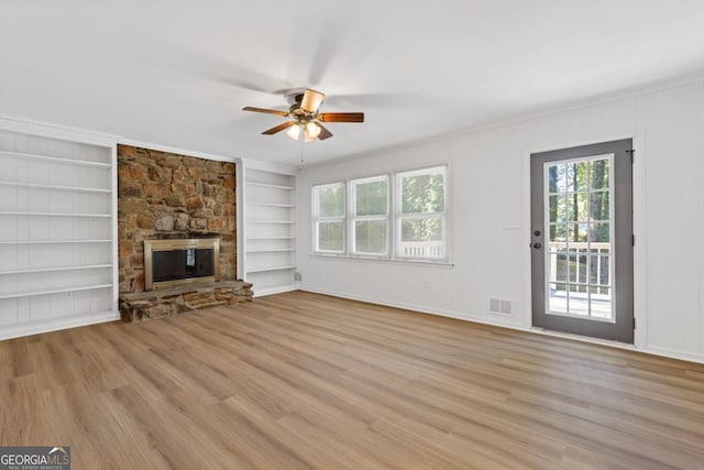 unfurnished living room with built in shelves, ceiling fan, a wealth of natural light, and a stone fireplace