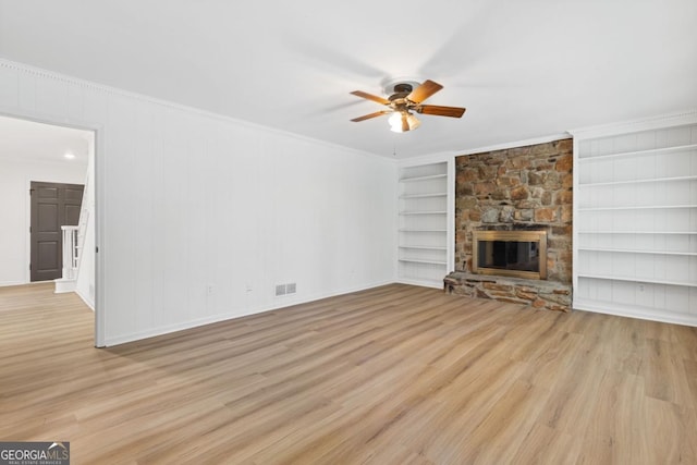 unfurnished living room featuring crown molding, light hardwood / wood-style flooring, ceiling fan, built in shelves, and a fireplace