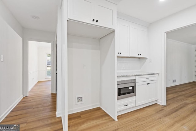 kitchen featuring stainless steel microwave, light stone countertops, light hardwood / wood-style floors, tasteful backsplash, and white cabinetry