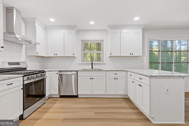 kitchen featuring wall chimney exhaust hood, sink, white cabinets, and appliances with stainless steel finishes