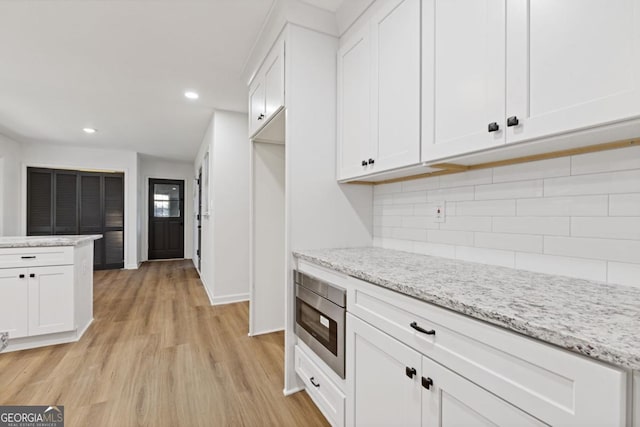 kitchen featuring light stone countertops, white cabinetry, decorative backsplash, stainless steel microwave, and light hardwood / wood-style flooring