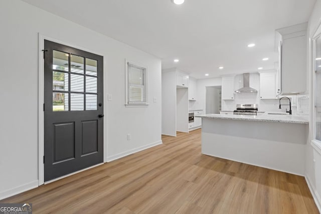 kitchen featuring white cabinetry, wall chimney range hood, sink, electric range, and light stone counters