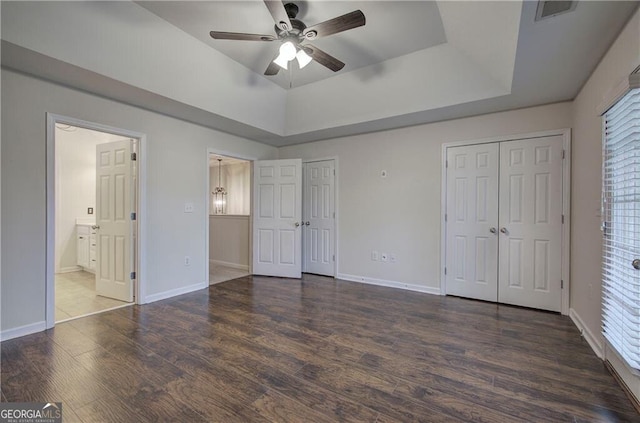 unfurnished bedroom featuring dark hardwood / wood-style flooring, two closets, ceiling fan, and a tray ceiling