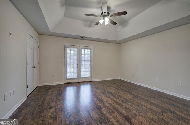 empty room featuring dark hardwood / wood-style floors, a raised ceiling, ceiling fan, and french doors